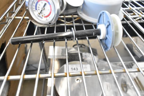 5 new scratch and dent items on a shelf, including light fixtures and a thermostat gauge with a visible reading and a lot tag.