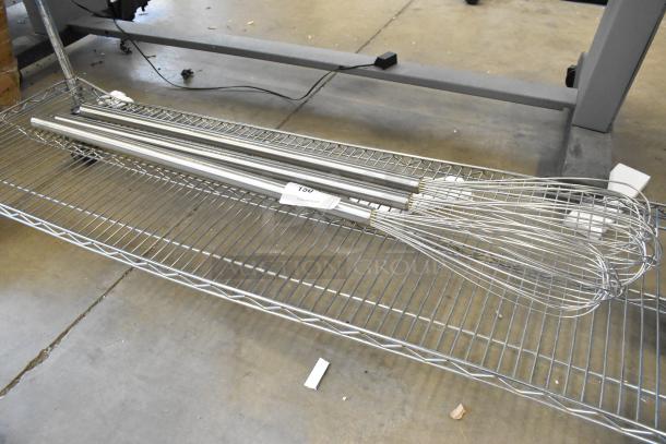 Three brand new metal mixing whisks with long handles on a shelf, labeled "T30" indicating scratch and dent condition.