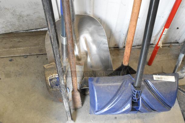 Lot of tools including a blue snow shovel, tamper, pole digger, and silver trash can. Items show signs of use.