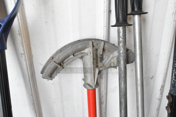 Lot of various tools including a metal tamper, pole digger, snow shovel, and trash can, in used condition.