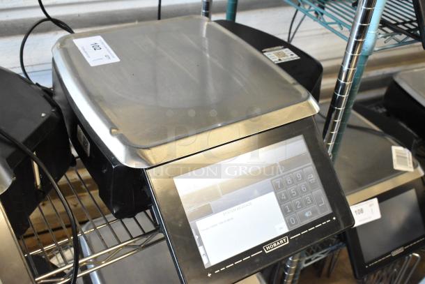 Hobart digital scale with keypad, stainless steel surface, model unknown, system message displayed, auction tag 102 visible.