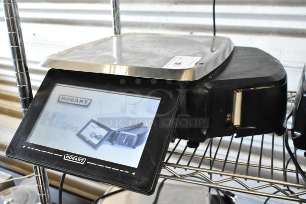 Hobart digital scale with touchscreen display, metal weighing platform, and model label. Slight wear visible.