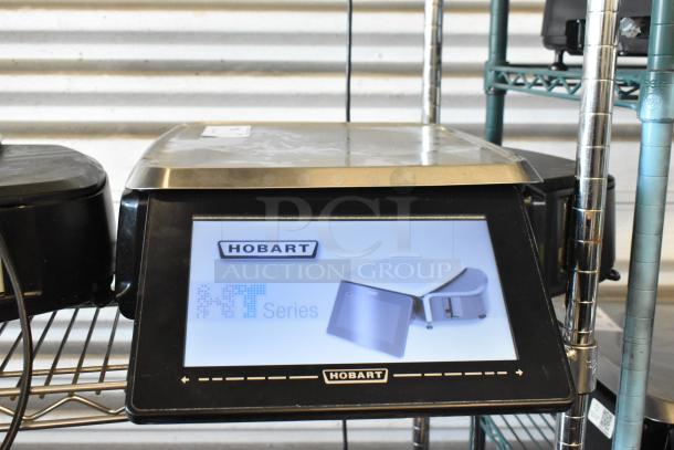 Hobart HT series digital scale, touchscreen display, metal casing, in good condition on a metal shelf.