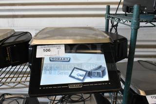Hobart NT Series touchscreen scale on metal shelf, model displayed. Auction tag 106 visible, indicating quantity of one.