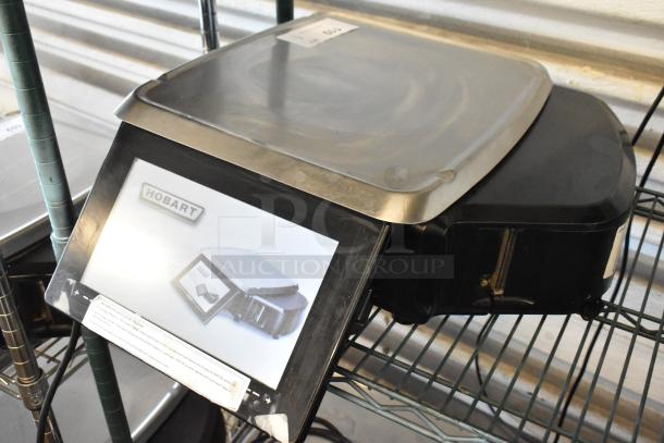 Hobart commercial food scale with stainless steel platform, model label visible, in used condition on metal shelving.