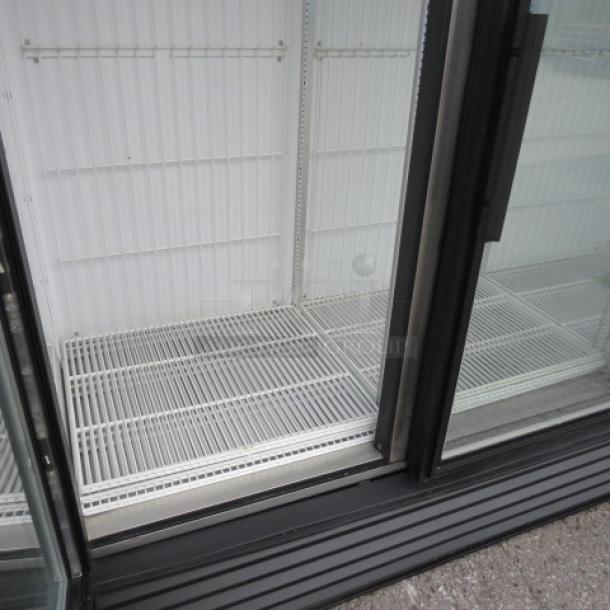 Commercial glass door refrigerator, empty, with clean white shelving. Sliding doors, black trim, good condition.
