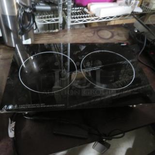 Black double-burner induction cooktop, glass surface, electric, good condition, caution label warns of hot surface.