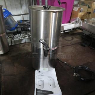 Stainless steel coffee urn with black spout, power cord attached, displayed with instruction manual on a countertop.