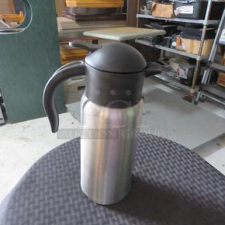 Stainless steel thermal carafe with black handle and lid, in good condition, designed for keeping beverages hot or cold.