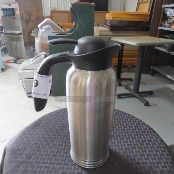 Stainless steel insulated carafe with black lid and handle, auction tag visible. Good condition, modern design.