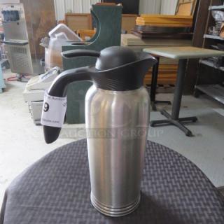 Stainless steel thermal carafe with black handle and spout, auction tag reading "Lot 9," in good condition.