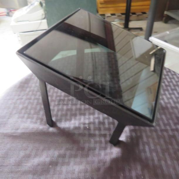 Black glass-topped coffee table with angled legs, in good condition. Reflective surface, modern design, approximately 20x15x18 inches.