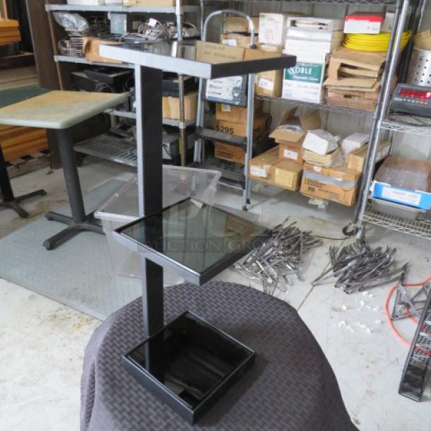Black metal display stand with three tiered glass shelves, showing minimal wear. Sturdy design, suitable for retail.