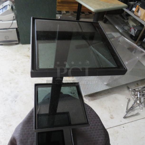 Black metal display stand with three glass shelves, square design, modern style, minimal wear, ideal for showcasing items.