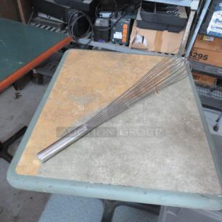 Large stainless steel whisk with long handle, in used condition, resting on a table. Ideal for commercial kitchens.