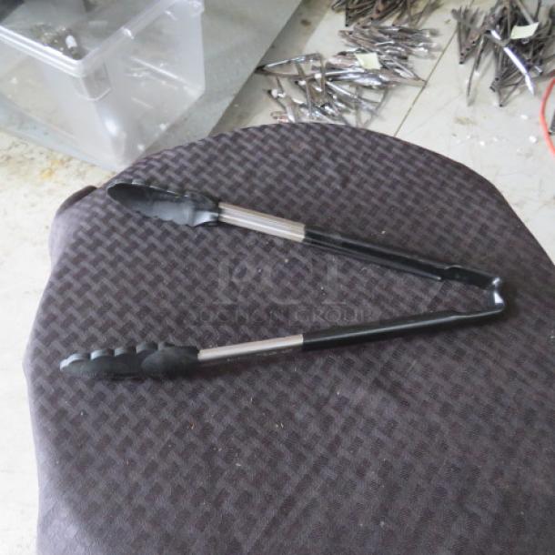 Metal and rubber kitchen tongs on a patterned surface, in good condition. Durable grip, suitable for cooking.