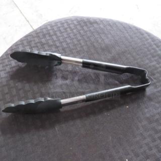 Black metal kitchen tongs with rubber grips on textured surface, showing minimal wear and no visible markings.
