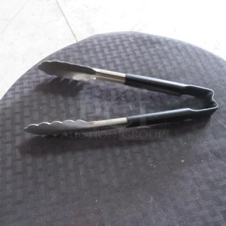 Stainless steel kitchen tongs with black rubber grips on a dark textured surface, in good condition.