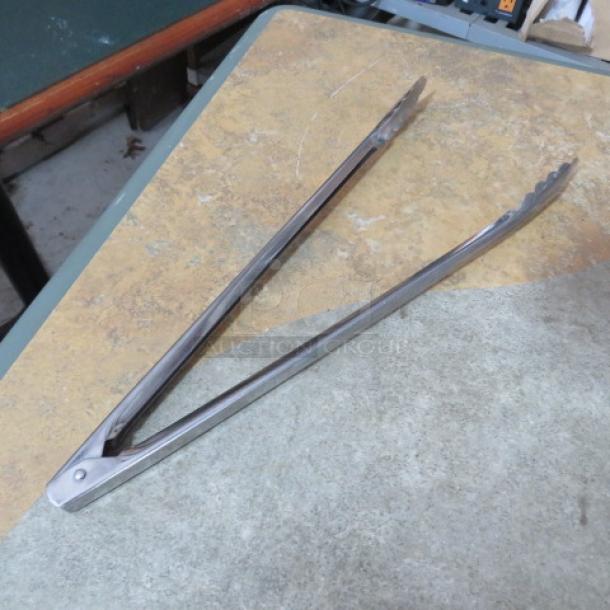 Metal serving tongs, stainless steel, serrated tip, used condition, minor surface wear. Ideal for kitchen or BBQ use.