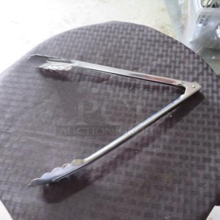 Stainless steel kitchen tongs with scalloped edges, resting on a dark surface. In good condition, showing minor wear.