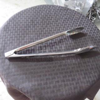 Stainless steel kitchen tongs on a dark textured surface, showing minimal wear. Long handles with scalloped tips.