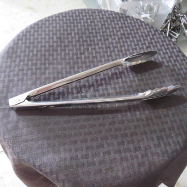 Stainless steel kitchen tongs on a table, in good condition, featuring a scalloped grip design.