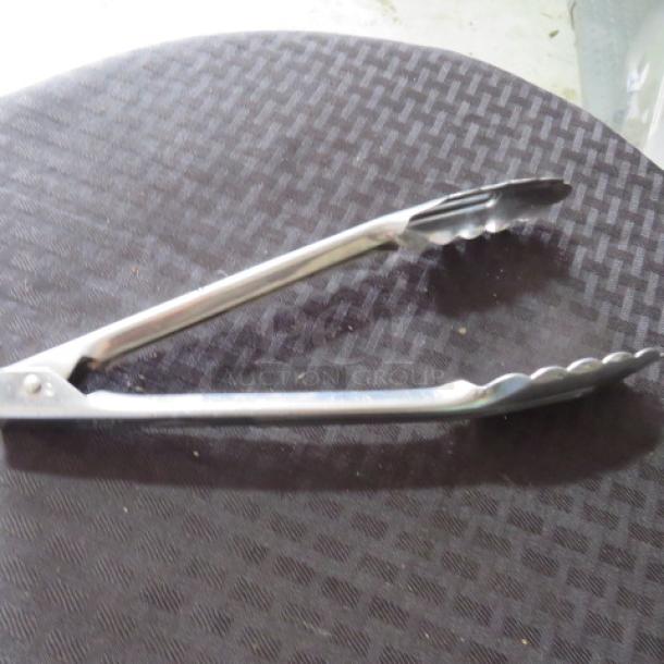 Stainless steel kitchen tongs in good condition, scalloped edges, silver color, suitable for cooking or serving.