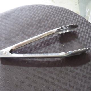 Stainless steel kitchen tongs in good condition, scalloped edges, silver color, suitable for cooking or serving.