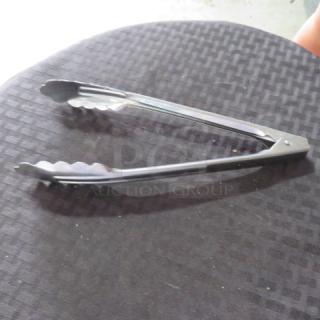 Metal kitchen tongs with scalloped edges, silver finish, in good condition, laid on a textured black surface.