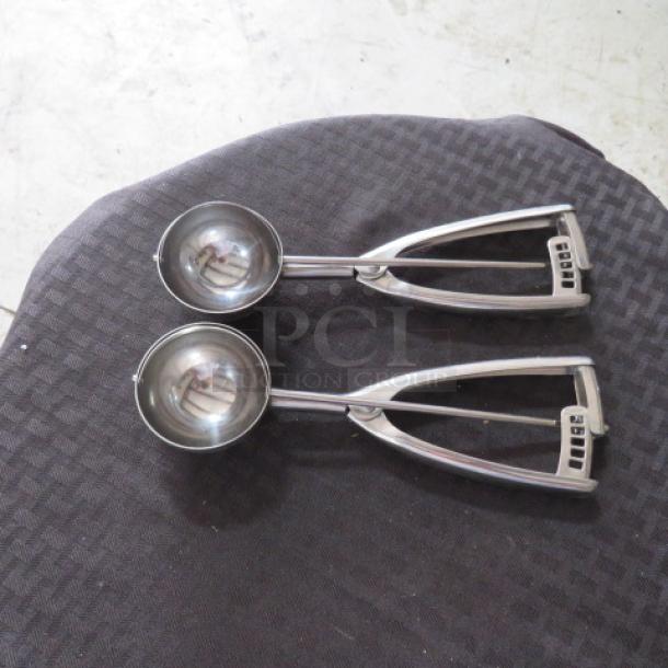 Two stainless steel ice cream scoops with spring-loaded handles, in good condition.
