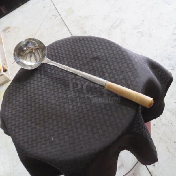 Stainless steel ladle with wooden handle on black cloth, in good condition. Ideal for kitchen use or collection.