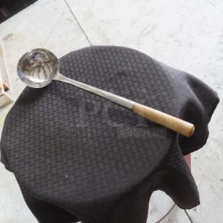 Stainless steel ladle with wooden handle on black cloth, in good condition. Ideal for kitchen use or collection.