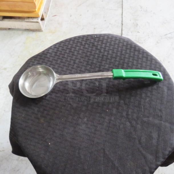 Stainless steel ladle with green handle, embossed with "Choice 2oz", on round black textured cloth. Excellent condition.