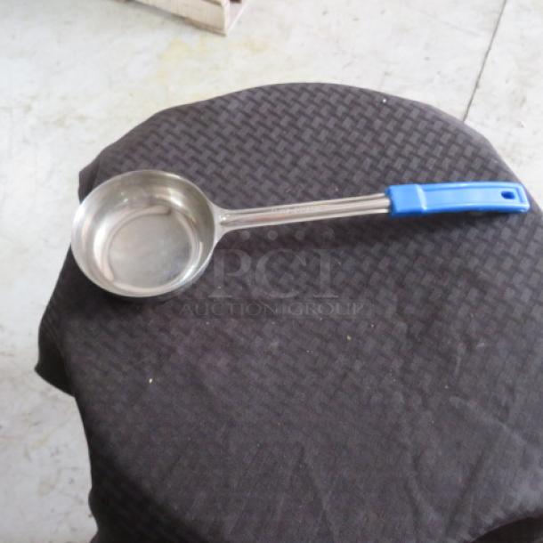 Stainless steel ladle with blue handle, used condition, resting on a dark fabric surface.