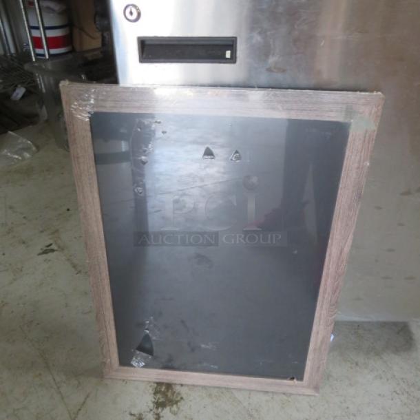 Wood-framed blackboard, medium size, minor surface scratches, protective film partially removed, leaning against a metal object.