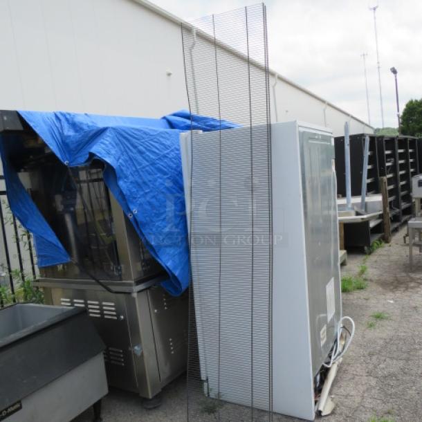 Commercial refrigerator and kitchen appliances outside, partially covered by a blue tarp. Apparent used condition.