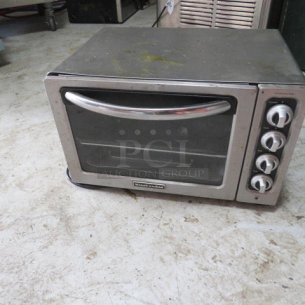 Stainless steel toaster oven with glass door and control knobs. Shows signs of wear and scratches. Brand visible: Black & Decker.