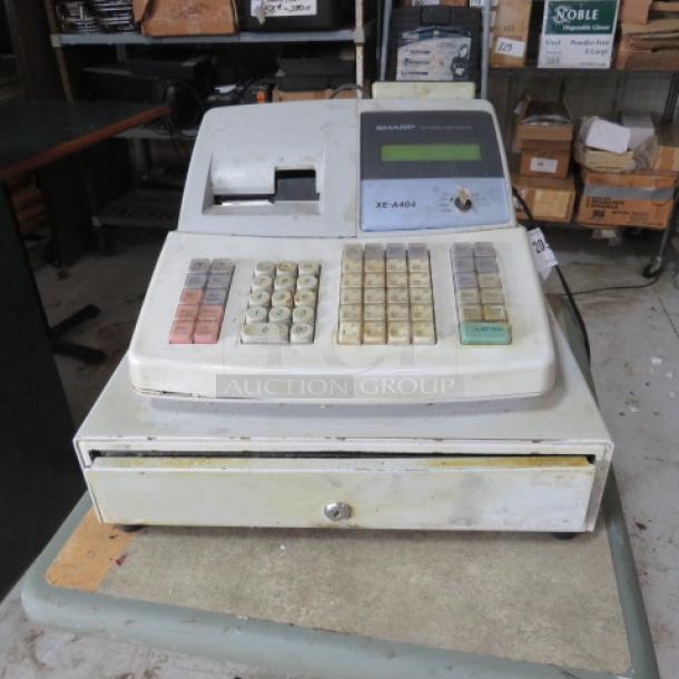 Vintage Sharp XE-A404 cash register, visible wear, numeric keypad, display screen, attached cash drawer, in used condition.