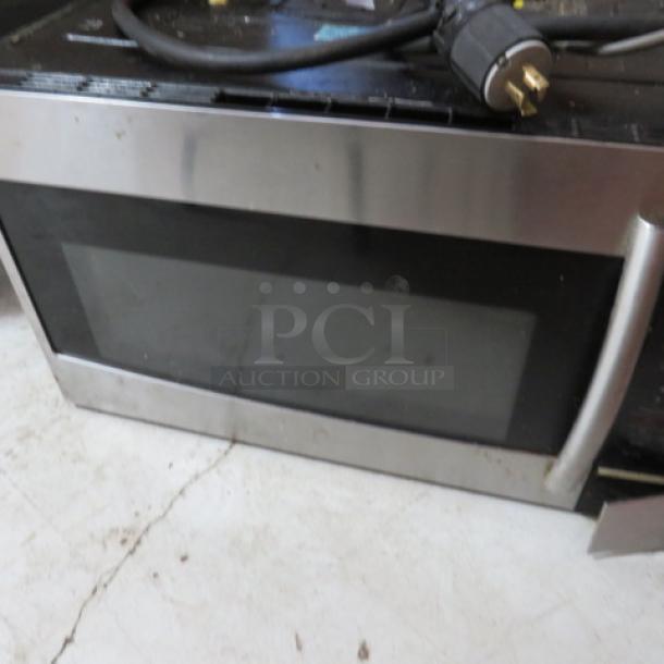 Stainless steel over-the-range microwave, used condition, with visible power cord and handle. No labels visible.