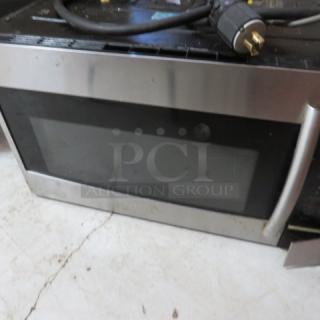 Stainless steel over-the-range microwave, used condition, with visible power cord and handle. No labels visible.