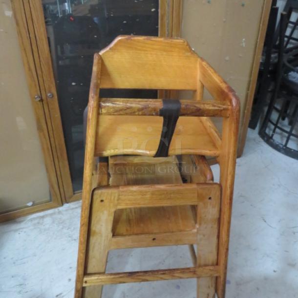 Wooden high chair with natural finish, black safety strap, minor wear. Sturdy design, ideal for vintage decor or restaurant use.