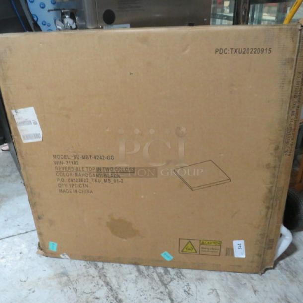 Cardboard box showing PDC:TXU02220915 marking, containing a reversible table top, colors mahogany/black, model XU-MBT-242-GG.
