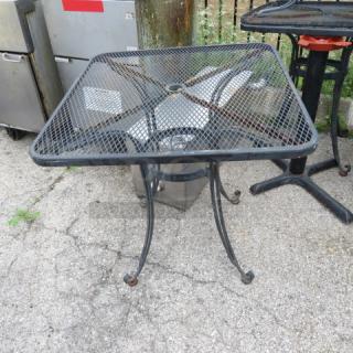 Square black metal mesh outdoor table with curved legs, showing signs of wear, suitable for patio or garden use.