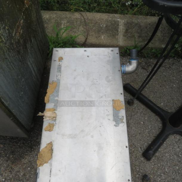 Metal panel with attached piping, visible wear and adhesive residue, outdoor setting. Potential industrial equipment piece.