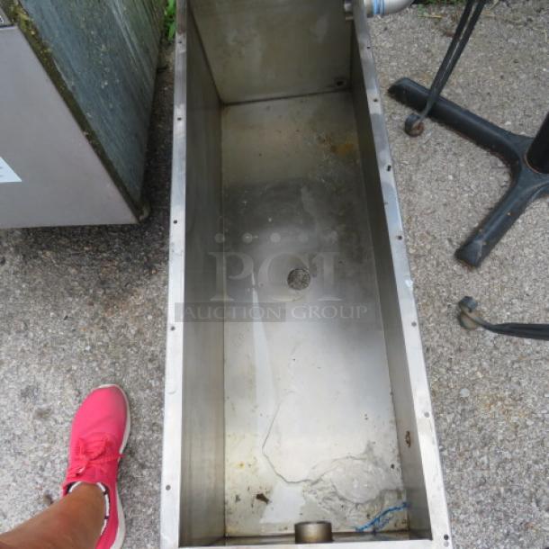 Stainless steel rectangular trough with drainage hole, used condition, visible wear and residue, outdoor placement.
