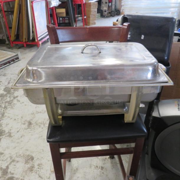 Stainless steel chafing dish with lid and gold-tone handles, showing minor wear. Ideal for catering or buffet use.