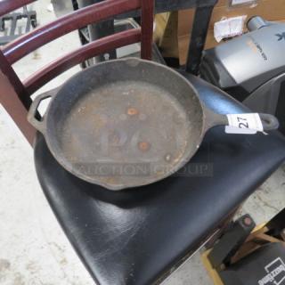 Vintage cast iron skillet with double handles, showing rust and wear, tagged with number 27 for auction.