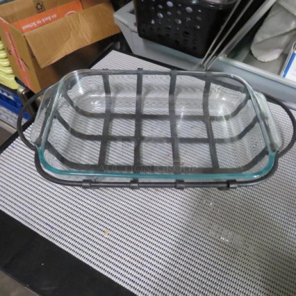 Glass baking dish with metal wire frame, rectangular, handles on sides, used condition, no visible markings or labels.