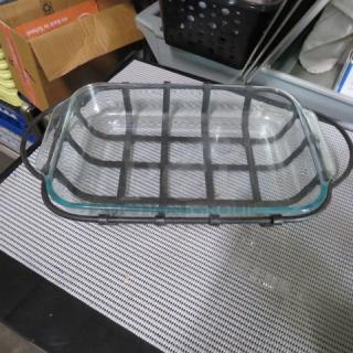 Glass baking dish with metal wire frame, rectangular, handles on sides, used condition, no visible markings or labels.