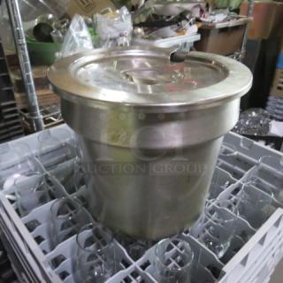 Large stainless steel commercial soup kettle with lid, situated in a dish rack. Some surface wear, indicating use.